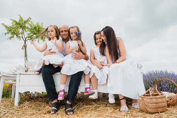 Fototapeta premium Family sitting on the picnic blanket in city park during weekend Sunday sunny day. Children are having fun playing.Happy cheerful family in nature, weekend.A plantation of blue flowers