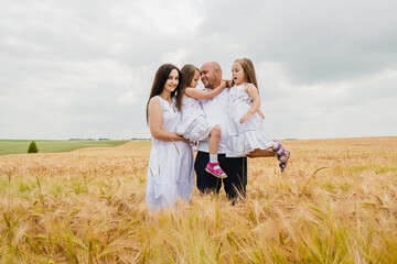 The concept of a friendly family.Mom, dad and daughters hug in a wheat field.Cute beautiful children.Family vacation.Happy family resting in summer park.Cheerful children picnicking in the park.
