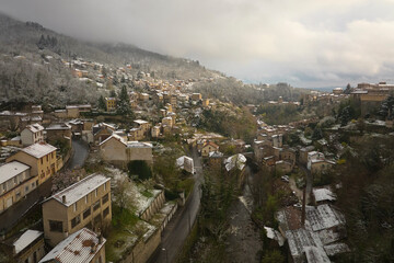 Aerial winter landscape of dense historic center of Thiers town in Puy-de-Dome department, Auvergne-Rhone-Alpes region in France. Rooftops of old buildings and narrow streets at snowfall