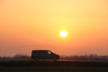Fototapeta na wymiar Passenger van driving fast on intercity road at sunset. Highway traffic in evening