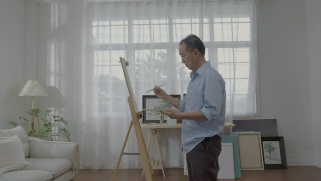 Artist concept of 4k Resolution. Asian man painting in the living room. Artist is creati