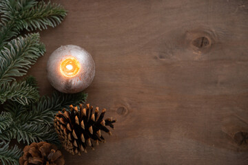 christmas decoration composition with burning candle, cone and lights on natural wooden background