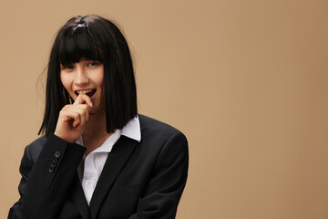 Pensive happy smiling pretty brunet lady in classic suit bites finger look at camera posing isolated on pastel beige studio background. Copy space Banner Offer. Pulp Fiction concept. Fashion Cinema