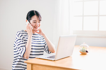 家でテレワークする日本人女性（スマホで電話）
