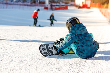 winter day, sitting snowboarder on the ski slope. snowboarder checks ammunition, checking fastening