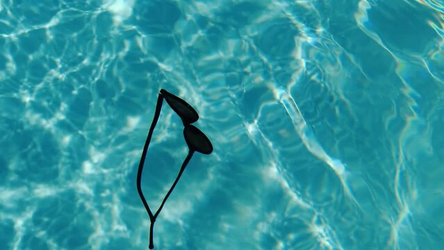 Sunglasses with blue lenses, inside the pool water. Summer, sunny day, lost objects.