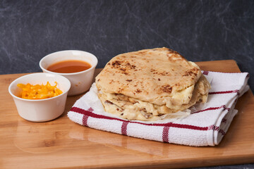 Pupusas on a wooden board with curtido and sauce over a black marble background