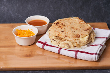 Pupusas on a wooden board with curtido and sauce over a black marble background
