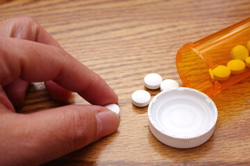 A man's hand is taking pills from an orange pill bottle on a wooden table, medicine pill on wooden table.