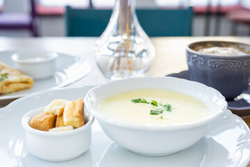 Morning breakfast with cheese soup, coffee, croutons, pancakes and greens against the background of backlight.