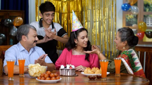 An old Indian lady feeding cake to her cheerful granddaughter - an Indian grandparent  a happy family. A teenage girl is spending time with her family during her birthday celebrations - three gener...