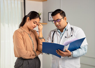 Indian man or male physician or doctor wearing stethoscope and apron holding a report file in hand and giving consultation to a tensed or worried female or Woman patient. Medical, medicine, healthcare