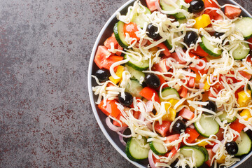 Traditional Shopska salad with vegetables, olives and cheese close-up in a plate on the table. Horizontal top view from above