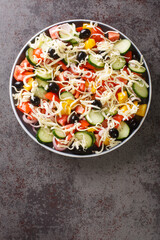 Shopska salad with tomatoes, cucumbers, onions, bell peppers, olives and cheese close-up in a plate on the table. Vertical top view from above