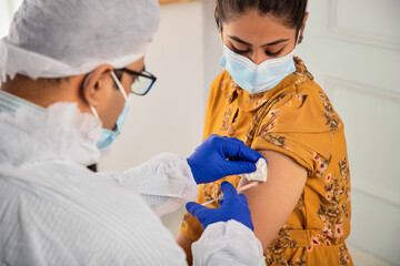 Close up of Indian male or man Doctor injecting a dose of vaccination dosage in arm of a young...