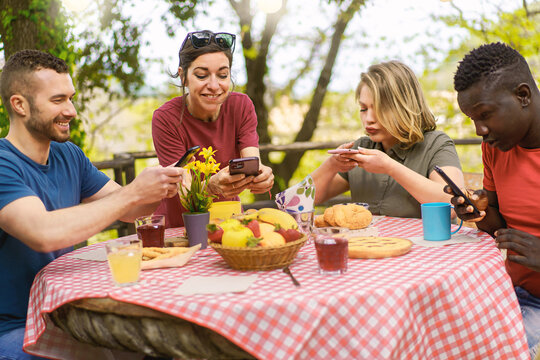 Group of multiethnic friends having fun taking pictures of food with mobile phones sitting together at picnic table for post sharing on social networks - food blogger and influencers wannabe concept