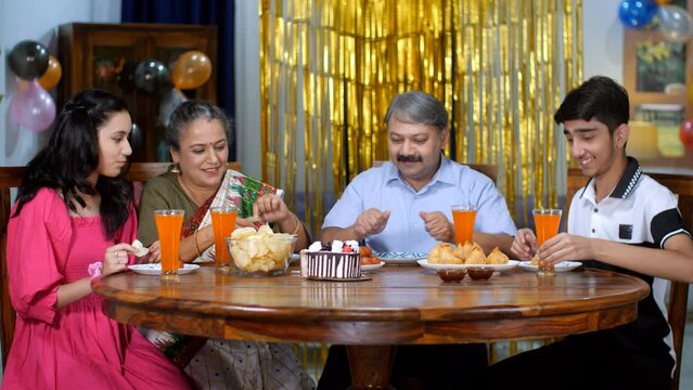 An Indian couple and their children doing a party at home - tasty snacks - delicious food  party time. Birthday party celebration at home - Joint family  Indian family  young kids  old parents  hap...