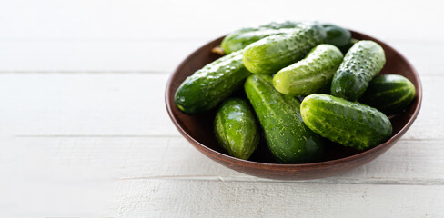 fresh cucumbers in a bowl on a white wooden background, banner, place for text