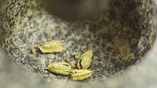 The cook crushing cardamom pods in a stone mortar.
