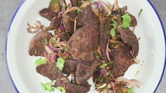 Chef sprinkling with coriander on fried liver served on a plate.
