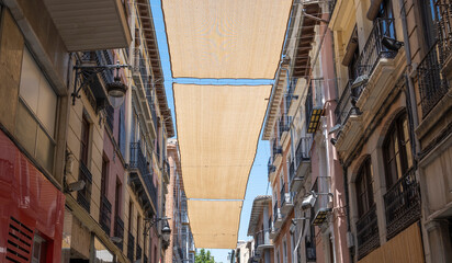 Fototapeta na wymiar Toldos de tela entre edificios para proteger del sol durante los días calurosos de verano en la ciudad de Granada, España