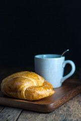 Butter croissant with a cup of coffee put on a wooden tray on a wooden floor.