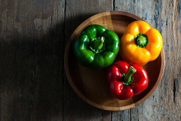 Colorful of bell peppers, green, red, yellow in a wooden tray on rustic wooden background, top view.