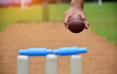Right hand of cricketer holds old red leather cricket ball, soft and selective focus on hand,...