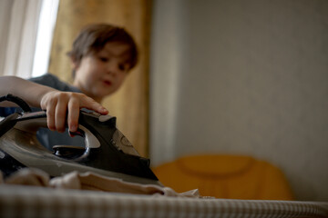 A five-year-old boy helps his parents around the house. A child ironing clothes, helping children around the house