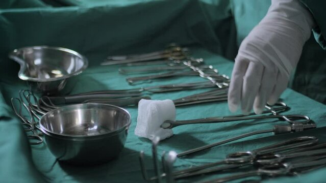 Close up shot of operation surgical equipment or instruments or tools like Scalpels, forceps, scissors, cotton and clamps tongs etc on the medical table being used by doctor or nurse in white gloves.