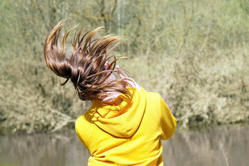 A girl in a yellow sweatshirt dances in nature