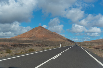 Una carretera vacía con un volcán al fondo en Lanzarote, Islas Canarias. Desierto árido con una...