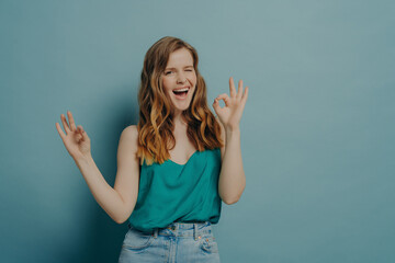 Fototapeta premium Charming funny girl shows OK sign with hands, winking and looking at camera with big smile