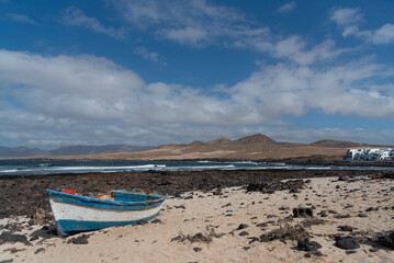 Fototapeta na wymiar Una barca de pesca abandonada en la arena de la playa con un volcán de fondo y edificios blancos en Lanzarote, isla canarias. 