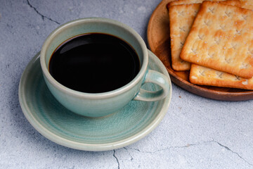 Hot black coffee in a green coffee cup with crackers.