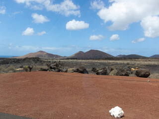 Paisaje natural volcánico con tierra negra y rocas y un gran volcán inactivo al fondo en Lanzarote, Islas Canarias en un día soleado con el cielo azul despejado. Parque Timanfaya. 