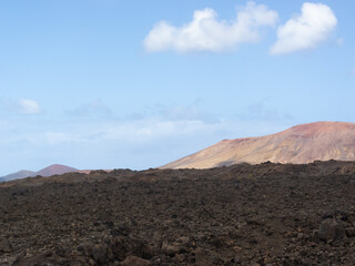 Paisaje volcánico y desértico con un gran volcán inactivo al fondo y rodeado de tierra y rocas negras durante un día soleado con el cielo azul despejado en Lanzarote Islas Canarias. Recursos naturales