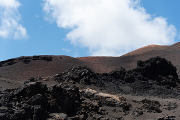 Paisaje volcánico y desértico con rocas y tierra negra con un camino cruzando los volcanes inactivos durante un día de verano en Lanzarote, Islas Canarias. Recursos turísticos y naturales.
