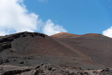 Paisaje volcánico y desértico en tonos marrones y anaranjados  con grandes volcanes inactivos al fondo durante un día de verano en Lanzarote, Islas Canarias. Recursos turísticos y naturales.