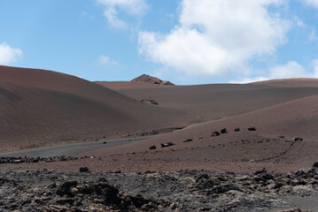 Paisaje volcánico y desértico con un camino cruzando los volcanes inactivos durante un día de verano en Lanzarote, Islas Canarias. Recursos turísticos y naturales.