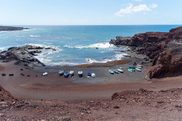 Fototapeta na wymiar Panorámica de Playa del Golfo en Lanzarote., de arena negra con unas barcas pesqueras azules junto a unos acantilados de roca volcánica al lado del mar turquesa un día soleado de verano Islas Canaria