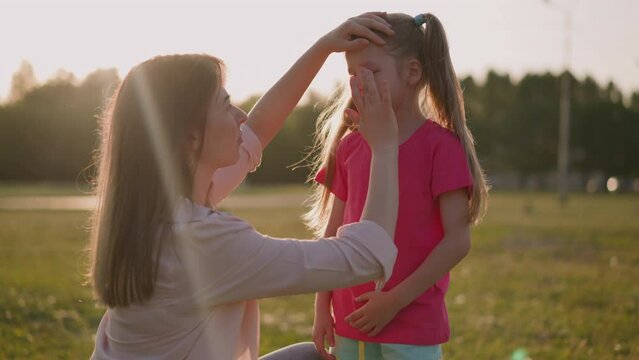 Mother applies decongestant cream onto swollen eyelid of little daughter in park. Insect bite allergic reaction. First air for hurt child