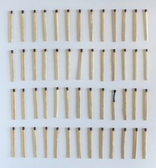 Four rows of identical matches on a white background. One match burned out. The concept of burnout, social difference, loneliness. View from above.