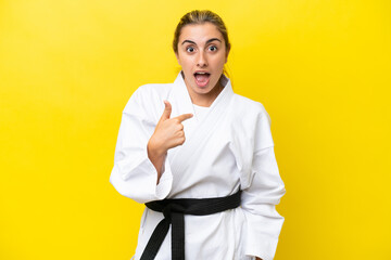 Young caucasian woman doing karate isolated on yellow background with surprise facial expression
