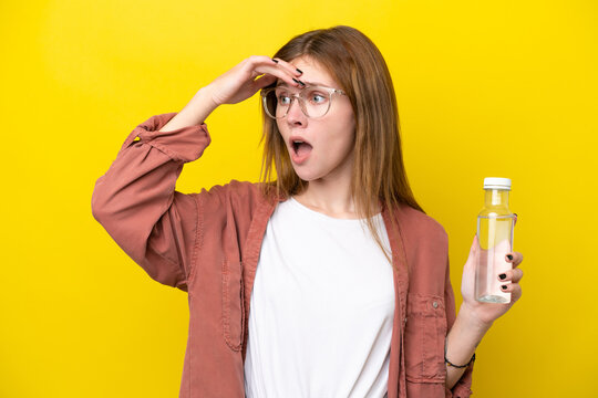 Young English woman with a bottle of water isolated on yellow background doing surprise gesture while looking to the side