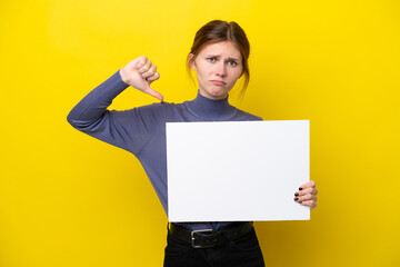Young English woman isolated on yellow background holding an empty placard and doing bad signal