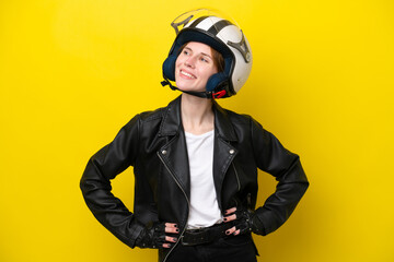 Young English woman with a motorcycle helmet isolated on yellow background posing with arms at hip and smiling