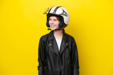 Young English woman with a motorcycle helmet isolated on yellow background looking to the side and smiling