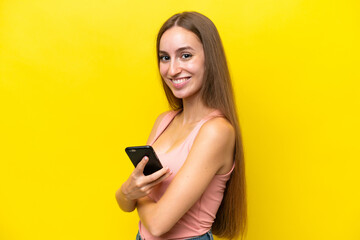 Young caucasian woman isolated on yellow background holding a mobile phone and with arms crossed