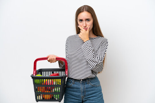 Young Rumanian woman holding a shopping basket full of food isolated on white background thinking